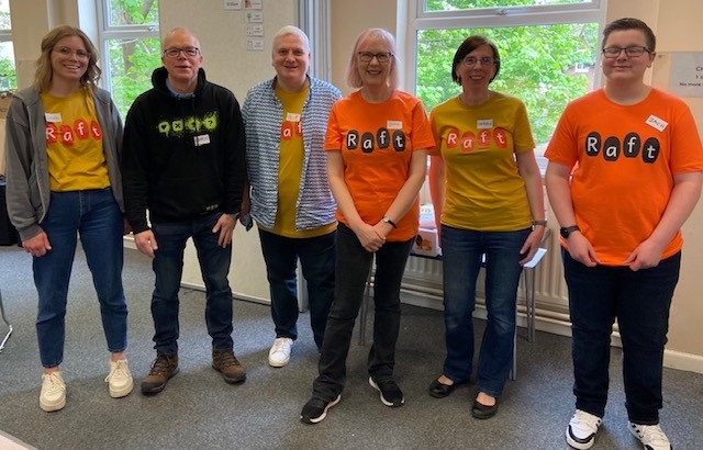 Six members of the Raft team stand in a line wearing orange and yellow 'Raft' t shirts. 